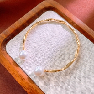 Close-up of a golden wavy bangle featuring elegant double pearls on a wooden tray