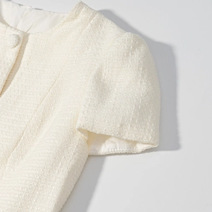 Dettaglio del top in tweed bianco che mostra la trama intrecciata e il bottone in tessuto