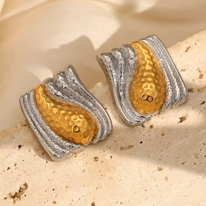 Macro shot of two-tone gold and silver bean stud earrings on a textured stone surface