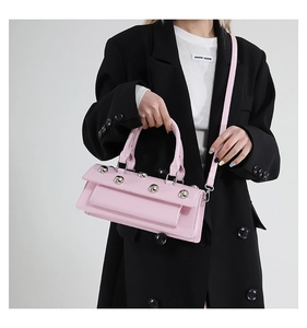 Pink glossy faux leather bag with silver rivets held by a model in a black blazer