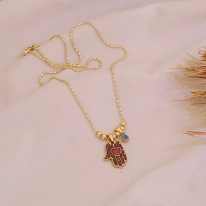Detailed view of gold Hamsa hand necklace with red heart and evil eye charm on fabric