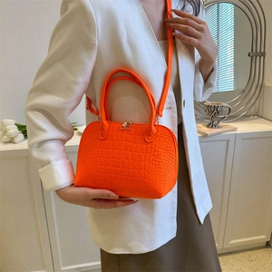 Orange croc-embossed shell handbag worn with white blazer for a stylish summer look