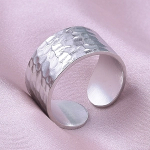 Detail of wide open ring featuring a hammered silver texture on pink satin fabric