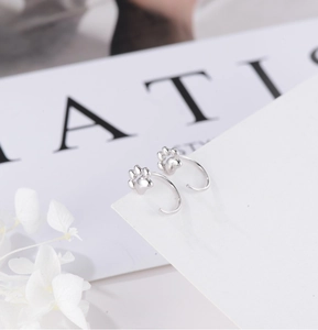 Detailed view of silver cat paw hook earrings on a minimalist decorative background