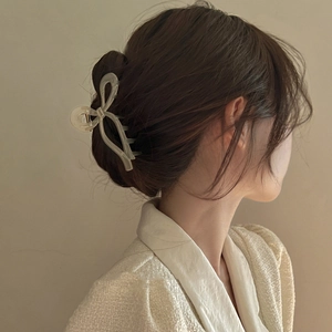 Detailed back view of a creamy white ribbon bow hair claw clip styled on a low hair bun