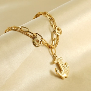 Detail of gold double-layered bracelet with anchor pendant on champagne satin background