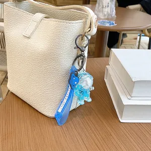 Blue astronaut quicksand bottle keychain hanging on an off-white textured handbag