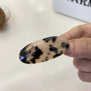 Macro view of handmade amber tortoise shell acetate hair clip with gold logo detail