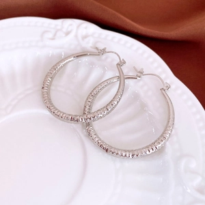Close-up of silver hoop earrings with textured stripes on white embossed porcelain