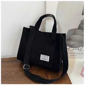 Detail of black corduroy handbag featuring white woven label and adjustable shoulder strap