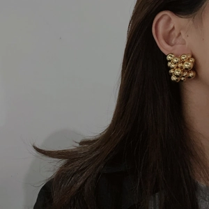 Close-up of golden metallic spherical cluster earrings worn on a model for a stylish look
