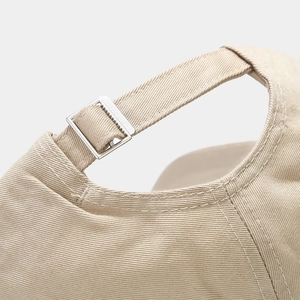 Detail of adjustable metal buckle and stitching on beige cotton baseball cap