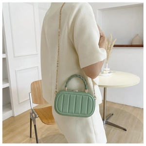 Detail view of grass green oval hard-shell box bag with vertical textures and gold chain