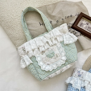 Detailed view of quilted plaid handbag with white lace trim and cute rabbit illustration