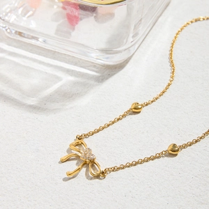 Close-up of gold bow pendant necklace with white diamonds and heart charms
