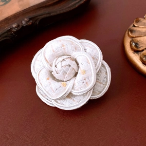 Detailed close-up of a white tweed camellia brooch with elegant gold sequin accents