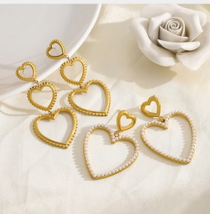 Detail view of gold tiered heart earrings and pearl-embellished heart studs on white plate