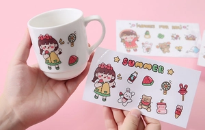 Close-up of cute cartoon stickers being applied to a white ceramic mug with pink background
