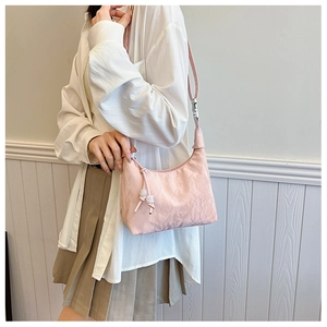 Détail d'un sac bandoulière plissé rose avec boucle argentée et pendentif décoratif