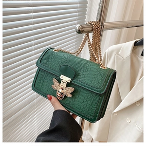 Detail of dark green embossed leather bag with gold bee buckle and metal chain
