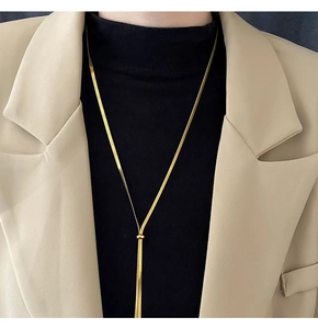 Close-up of golden snake chain sweater necklace worn over a beige suit jacket