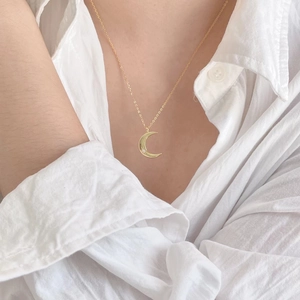 Close-up of a minimalist gold crescent moon pendant necklace with a small center zircon