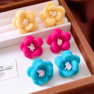 Close-up of wool-felt flower earrings in yellow, pink, and blue within a jewelry box