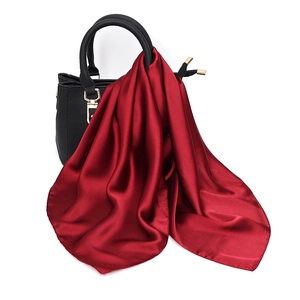 Detail of elegant burgundy silk scarf tied on a handbag showing smooth satin texture