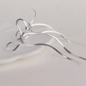 Minimalist silver stainless steel bow earrings on a white shell decorative tray