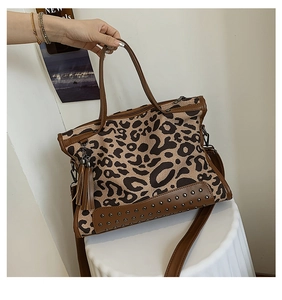 Detail view of leopard print canvas bag with brown leather trim and tassel accent