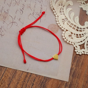 Red braided rope bracelet with golden heart pendant on vintage letter background