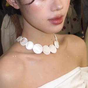Close-up of a white shell choker necklace with round iridescent discs on a female model