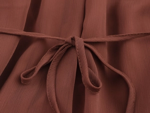 Dettaglio della cintura in vita e della trama in chiffon su un abito lungo color ruggine