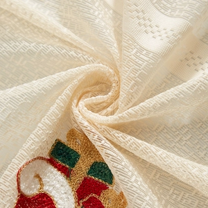 Detailed view of festive embroidery on semi-transparent cream lace curtain fabric