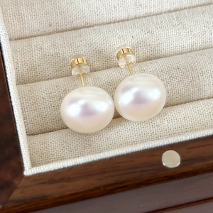 Close-up of white freshwater pearl earrings with gold posts on a wooden display