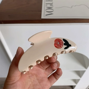Detail of beige tulip claw clip with red floral and swallow pattern in a hand-held view