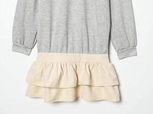 Detail aus grauem Strickstoff mit beigem, gestuftem Volant-Saum an einem Kleid