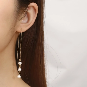 Close-up of elegant gold tassel earrings with three white pearls on a fine metal chain