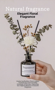Close-up of 50ml reed diffuser with eucalyptus leaves and a white sola flower held by hand