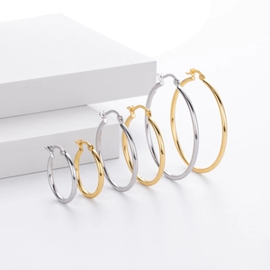 Multiple sizes of minimalist hollow gold and silver hoop earrings on a white platform