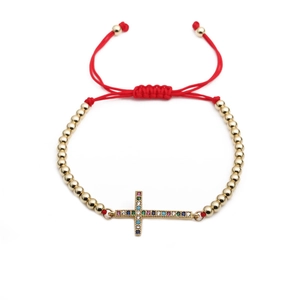 Bracelet tressé rouge avec croix en zircon coloré et billes dorées sur fond blanc
