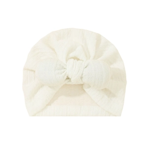 Close-up of white knit baby turban hat with delicate bow and jacquard texture