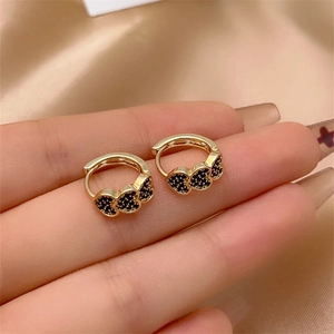 Macro shot of gold hoop earrings with three linked black pavé-set hearts on champagne satin