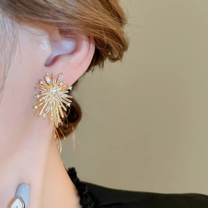 Detailed close-up of golden firework zircon stud earrings worn on model's ear