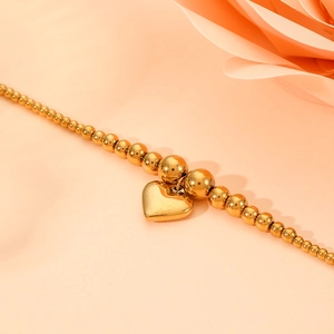 Elegant gold stainless steel beaded bracelet with a heart pendant on a warm background