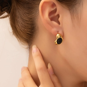Close-up of a gold teardrop earring with black onyx stone on an elegant female model