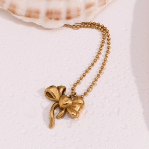 Detail of 18K gold plated bow pendant on bead chain against shell and water background