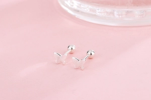 Macro shot of silver butterfly screw back earring showing metal texture on pink background