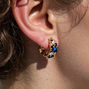 Close-up of gold hoop earring with navy blue and clear stones on a female model