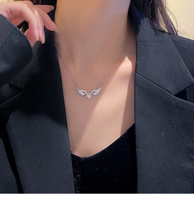 Close-up of angel wing necklace with heart cubic zirconia on woman in black blazer